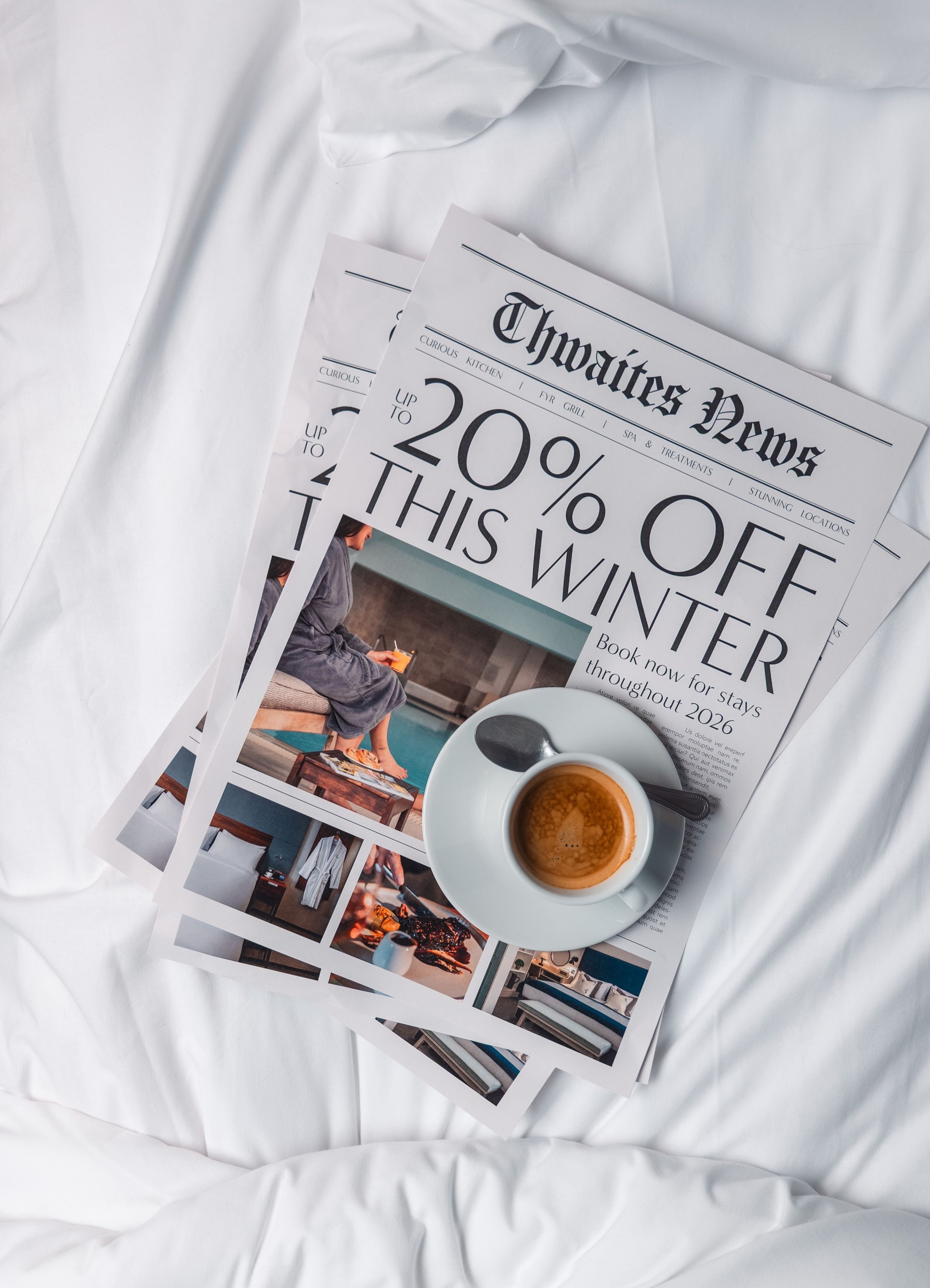 Newspaper and coffee on hotel bed that reads "Up to 20% off this winter"